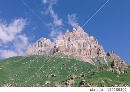Mount Naudzhidza rocky peak above green alpine meadow under blue sky Mount Naudzhidza rocky peak above green alpine meadow under blue sky 139589301