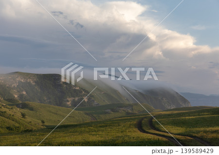 Mountain meadow road with low clouds over Caucasus ridge in Dagestan region 139589429