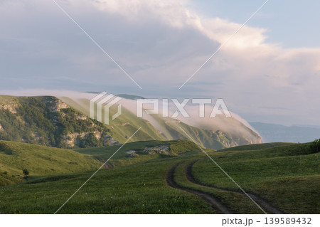 Fog over mountain ridges and dirt road in Dagestan highlands at sunrise Fog over mountain ridges and dirt road in Dagestan highlands at sunrise 139589432