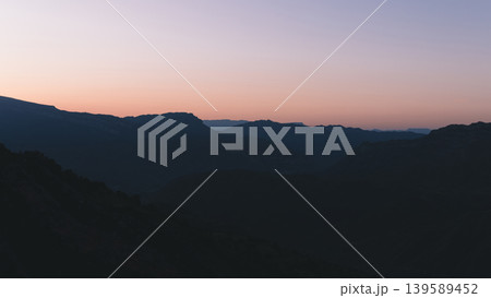 Mountain silhouettes at sunrise over Dagestan valley with pastel sky and haze Mountain silhouettes at sunrise over Dagestan valley with pastel sky and haze 139589452