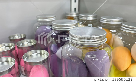 Clear plastic jars with silver lids filled with colorful makeup sponges on a store display shelf Clear plastic jars with silver lids filled with colorful makeup sponges on a store display shelf 139590122