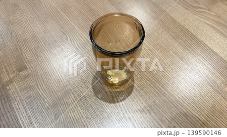 Top view of a single amber glass tumbler on a light wooden table surface with soft shadows 139590146
