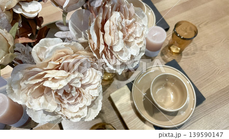 Top view of an elegant table setting with beige ceramic plates, amber glassware, decorative candles, and soft pink peonies on a wooden surface Top view of an elegant table setting with beige ceramic plates, amber glassware, decorative candles, and soft pink peonies on a wooden surface 139590147