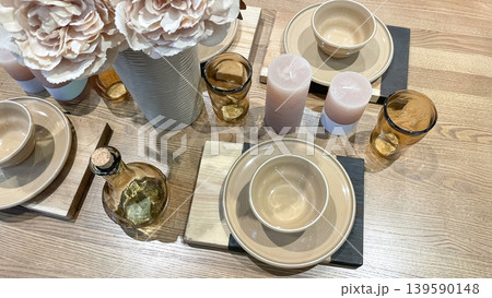 Top view of an elegant table setting with beige ceramic plates, amber glassware, decorative candles, and soft pink peonies on a wooden surface Top view of an elegant table setting with beige ceramic plates, amber glassware, decorative candles, and soft pink peonies on a wooden surface 139590148