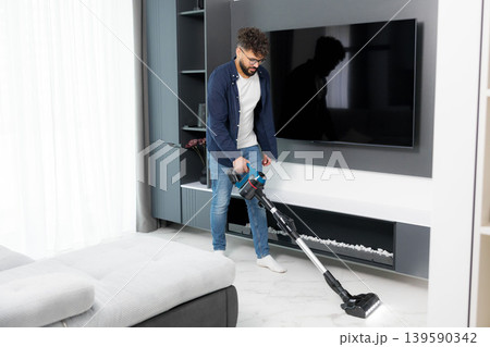 Young man cleaning living room floor with cordless vacuum Young man cleaning living room floor with cordless vacuum 139590342