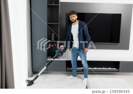 Young man cleaning living room using stick vacuum cleaner Young man cleaning living room using stick vacuum cleaner 139590345