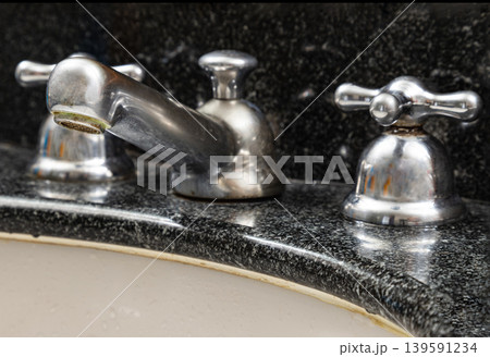 Viewed from a striking side profile, the vintage-inspired mixer faucet rises gracefully from a deep, star-speckled granite canvas, its classic cross-handles capturing subtle reflections. Viewed from a striking side profile, the vintage-inspired mixer faucet rises gracefully from a deep, star-speckled granite canvas, its classic cross-handles capturing subtle reflections. 139591234