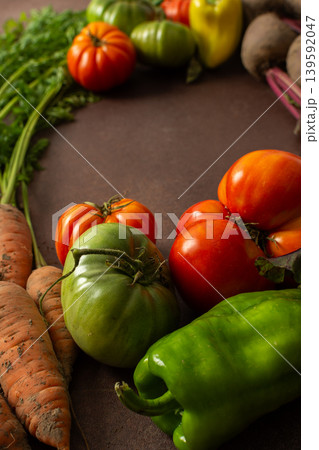 Fresh carrots sit next to red and green tomatoes along with bell peppers on a brown surface. The scene shows a variety of vegetables gathered for cooking or selling 139592047