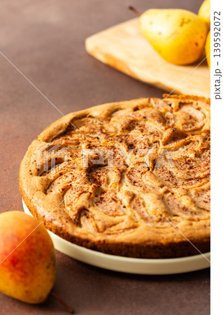 A fresh pear pie is placed on a cloth on a table. Nearby, a bowl holds ripe pears and a small vase has flowers. The setting looks warm and inviting for sharing a treat A fresh pear pie is placed on a cloth on a table. Nearby, a bowl holds ripe pears and a small vase has flowers. The setting looks warm and inviting for sharing a treat 139592072