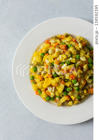 This colorful salad combines boiled eggs, tender chicken breast, diced potatoes, vibrant carrots, and green peas, all drizzled with rich olive oil for a nutritious meal 139592395