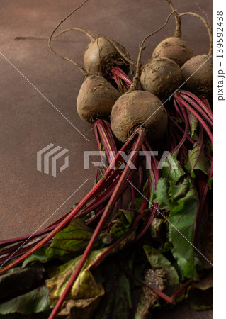 Beets with green leaves rest on a brown surface in a kitchen. The setting is warm and hints at fresh produce ready for cooking or eating 139592438