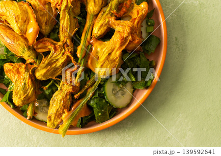 Roasted zucchini flowers are placed on a bed of fresh greens, cucumbers, and broccoli during a summer meal. This dish highlights the flavors of summer ingredients 139592641