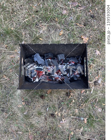Hot coals in portable grill, close up of campfire on dry grass during outdoor camping Hot coals in portable grill, close up of campfire on dry grass during outdoor camping 139593004