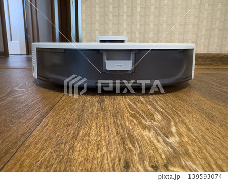White robot vacuum cleaner on wooden floor, smart home cleaning device close-up in modern apartment interior White robot vacuum cleaner on wooden floor, smart home cleaning device close-up in modern apartment interior 139593074
