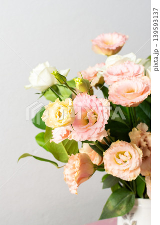A bouquet of fresh flowers is arranged in a white pitcher on a pink surface. The flowers include pink and white blooms along with green leaves, seen in good light A bouquet of fresh flowers is arranged in a white pitcher on a pink surface. The flowers include pink and white blooms along with green leaves, seen in good light 139593137