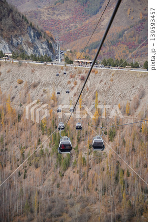 Cable car gondolas moving over autumn mountain forest in Shymbulak, Kazakhstan. 139593457
