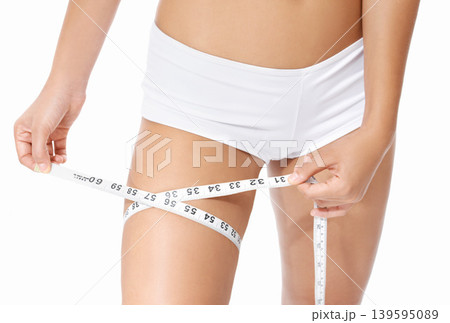 Woman, legs and tape measure for diet, weight loss or slim body in health and wellness on a white studio background. Closeup of female person or model hands measuring thigh in fitness or healthcare Woman, legs and tape measure for diet, weight loss or slim body in health and wellness on a white studio background. Closeup of female person or model hands measuring thigh in fitness or healthcare 139595089