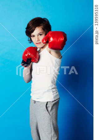 Portrait, boy and kid with boxing gloves, fitness and confident fist on a blue studio background. Child development, punch and fighting with workout, combat and training with fun and mockup space 139595310