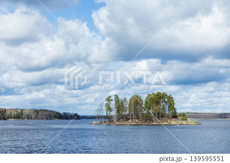 A small rocky island sits in a calm lake beneath dramatic cloudy skies. Karelia 139595551