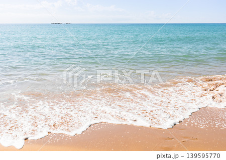 Calm ocean waves gently lapping on sandy beach under clear blue sky Calm ocean waves gently lapping on sandy beach under clear blue sky 139595770