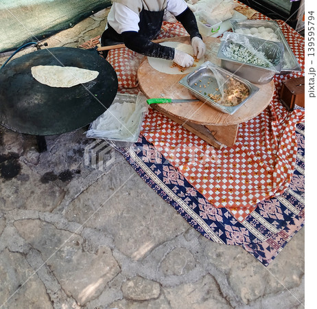 Street vendor preparing traditional flatbread on outdoor cooking surface 139595794