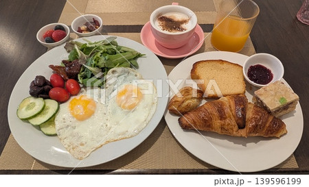 Large breakfast plates with bread, fried eggs, salad, nuts, fruits, and drinks 139596199