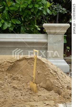 Pile of sand with a shovel in the foreground, set against a decorative Thai Buddhist temple fence in the background Pile of sand with a shovel in the foreground, set against a decorative Thai Buddhist temple fence in the background 139596625