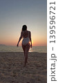 Woman in white swimsuit walking on beach to sunset over sea 139596721