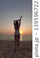 Woman in white swimsuit walking on beach to sunset over sea 139596722