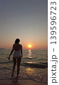Woman in white swimsuit walking on beach to sunset over sea 139596723