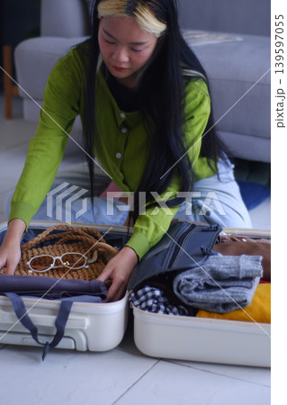Young Asian women folding clothes, packing luggage for holiday trip. Young Asian women folding clothes, packing luggage for holiday trip. 139597055