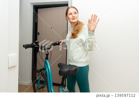 A woman leaves an apartment with a bicycle A woman leaves an apartment with a bicycle 139597112