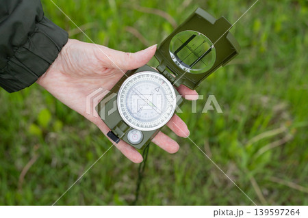 Woman's hand displays the dial of a well-worn compass against a background of green grass. Concept of travel, adventure Woman's hand displays the dial of a well-worn compass against a background of green grass. Concept of travel, adventure 139597264