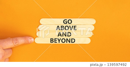 Go above and beyond symbol. Concept words Go above and beyond on beautiful wooden sticks. Beautiful orange background. Businessman hand. Business motivational Go above and beyond concept. Copy space. Go above and beyond symbol. Concept words Go above and beyond on beautiful wooden sticks. Beautiful orange background. Businessman hand. Business motivational Go above and beyond concept. Copy space. 139597492