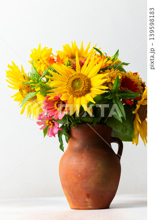 Flowers in a vase fill a space with color and texture. Sunflowers, zinnias, and greenery are mixed together. Light brightens the scene, showcasing their vibrant colors Flowers in a vase fill a space with color and texture. Sunflowers, zinnias, and greenery are mixed together. Light brightens the scene, showcasing their vibrant colors 139598183
