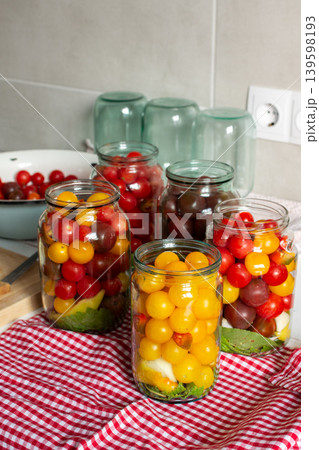 In a kitchen, jars filled with canned tomatoes sit on a table beside fresh vegetables. A mixing bowl holds whole tomatoes as preparation for winter storage continues In a kitchen, jars filled with canned tomatoes sit on a table beside fresh vegetables. A mixing bowl holds whole tomatoes as preparation for winter storage continues 139598193