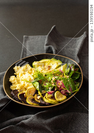 A bowl contains millet porridge next to baked zucchini and beets. There is a salad made of spinach, arugula, and pink radish with nuts and seeds. The setting is simple and clean A bowl contains millet porridge next to baked zucchini and beets. There is a salad made of spinach, arugula, and pink radish with nuts and seeds. The setting is simple and clean 139598194