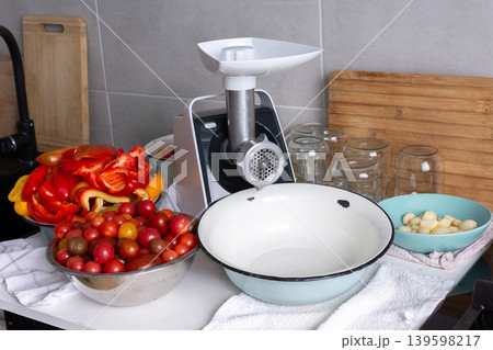 A person is in the kitchen preparing for winter by making Adjika. Fresh vegetables are in bowls and a grinder is ready for use. Jars are available for storing the seasoning A person is in the kitchen preparing for winter by making Adjika. Fresh vegetables are in bowls and a grinder is ready for use. Jars are available for storing the seasoning 139598217