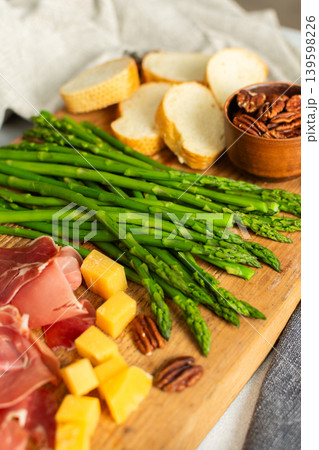 Indulge in a beautifully arranged charcuterie board with vibrant asparagus, savory cured meats, assorted cheeses, and freshly toasted bread, ideal for sharing with friends Indulge in a beautifully arranged charcuterie board with vibrant asparagus, savory cured meats, assorted cheeses, and freshly toasted bread, ideal for sharing with friends 139598226