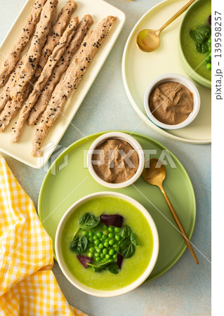 A bowl of creamy broccoli and green pea soup sits on a green plate. Next to it is liver pate in a small dish and grissini on a white platter. This meal provides healthy options A bowl of creamy broccoli and green pea soup sits on a green plate. Next to it is liver pate in a small dish and grissini on a white platter. This meal provides healthy options 139598257