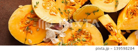 Pumpkin slices are arranged on a kitchen counter with fresh herbs nearby. The scene shows the preparation of seasonal dishes in the fall, banner 139598284
