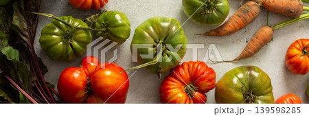 Various types of tomatoes and carrots are placed together on a flat surface. The assortment shows green and ripe tomatoes along with leafy greens and roots, banner Various types of tomatoes and carrots are placed together on a flat surface. The assortment shows green and ripe tomatoes along with leafy greens and roots, banner 139598285