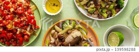 Breakfast includes baked hake placed on boiled beans with broccoli and peppers. A fresh tomato salad and lime water are nearby on a green table, banner 139598288