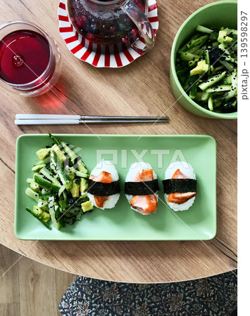 Food is arranged on a green plate with salad made of nori, cucumbers, and avocado alongside nagiri sushi topped with red fish, suitable for breakfast or lunch 139598297