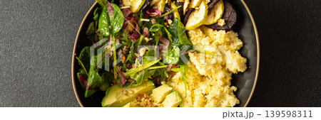 A bowl contains millet porridge next to baked zucchini and beets. There is a salad made of spinach, arugula, and pink radish with nuts and seeds. The setting is simple and clean, banner 139598311