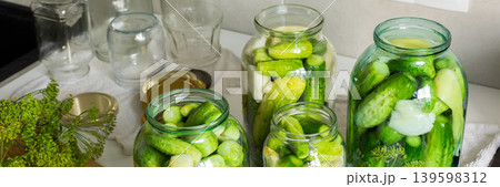 Cucumbers are being prepared and placed into glass jars for canning in a kitchen. The process helps preserve cucumbers for winter use, ensuring they last longer, banner 139598312