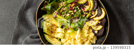 A bowl contains millet porridge next to baked zucchini and beets. There is a salad made of spinach, arugula, and pink radish with nuts and seeds. The setting is simple and clean, banner 139598315