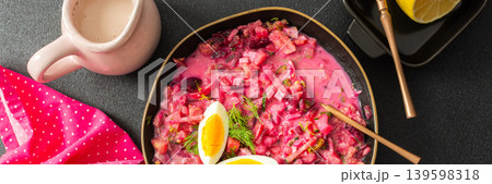 A colorful bowl of beet soup features chopped vegetables, sliced eggs, and fresh herbs. The setting includes a jug of cream, a lemon, and radishes, creating a cozy atmosphere, banner A colorful bowl of beet soup features chopped vegetables, sliced eggs, and fresh herbs. The setting includes a jug of cream, a lemon, and radishes, creating a cozy atmosphere, banner 139598318