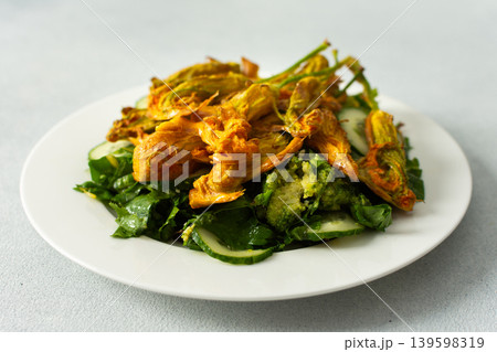 Roasted zucchini flowers sit on a bed of salad made with fresh greens, cucumbers, and broccoli. This dish highlights summer flavors and healthy eating options 139598319