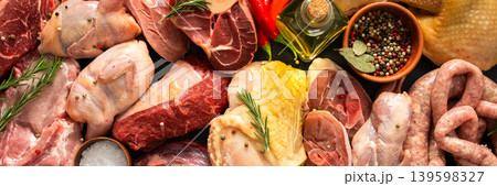 Various cuts of meat are arranged on a dark surface. Beef steaks, quail, pork sausages, turkey, chicken, and pork are present along with herbs and spices, banner Various cuts of meat are arranged on a dark surface. Beef steaks, quail, pork sausages, turkey, chicken, and pork are present along with herbs and spices, banner 139598327